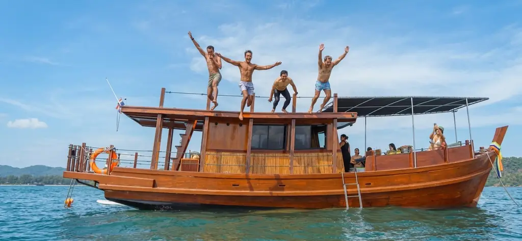 Four guests leaping from the roof of the Endless Summer Thai teak cruiser into clear blue water